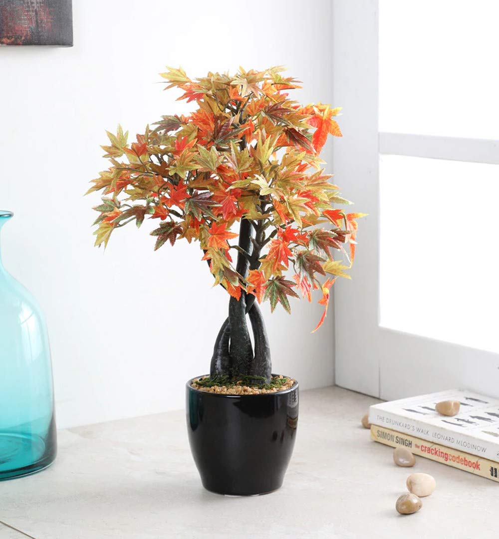 Artificial bonsai tree with autumn leaves in a black pot on a white surface.