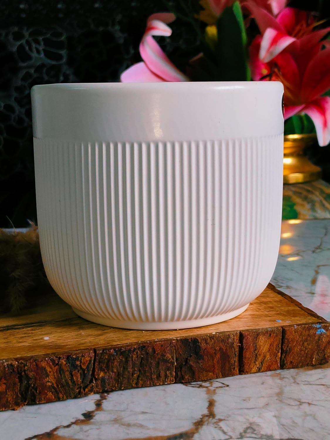 White ceramic pot on a wooden surface with blurred flowers in the background