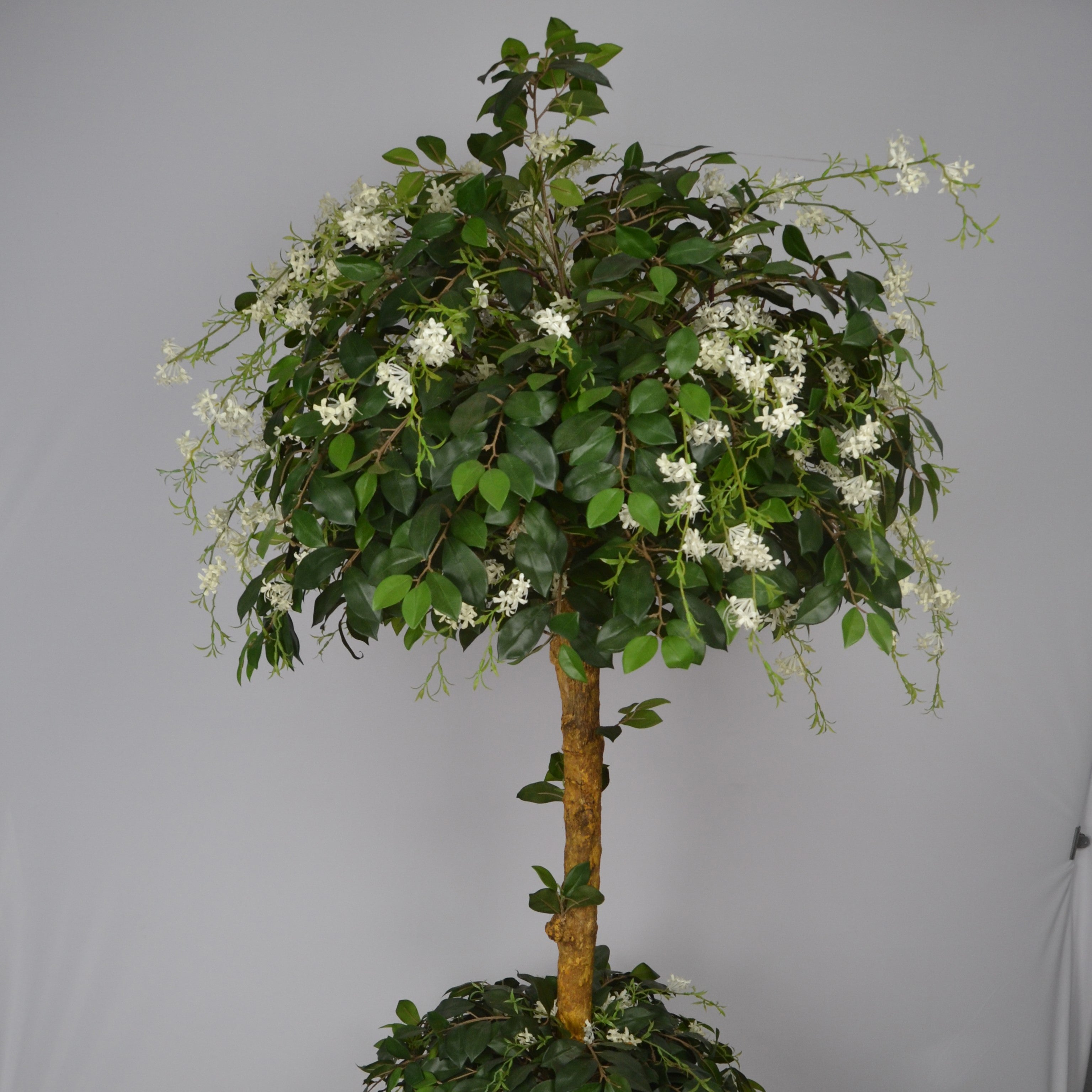 Artificial topiary tree with green leaves and white flowers on a gray background