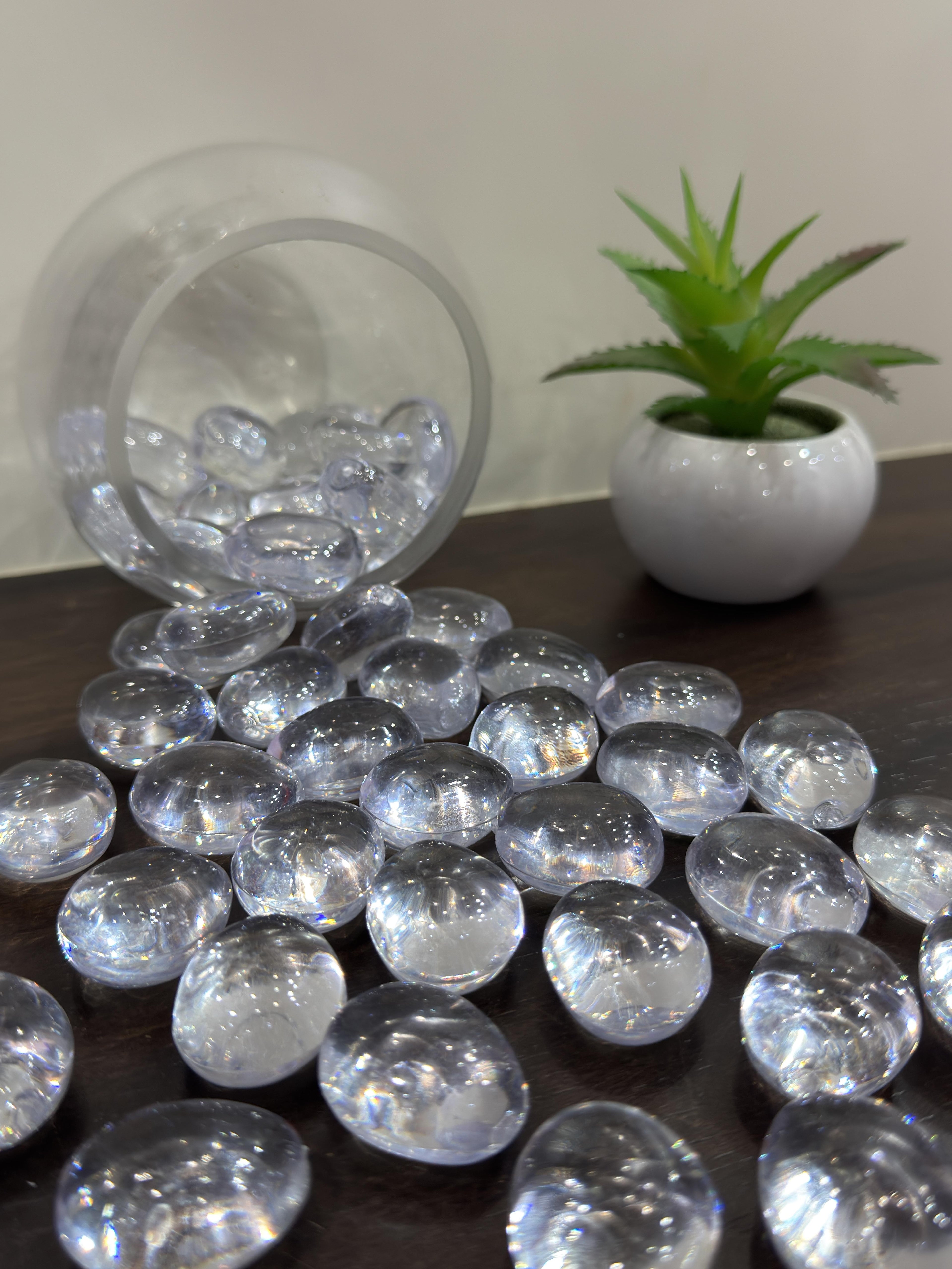 Clear decorative stones on a dark surface with a potted plant in the background
