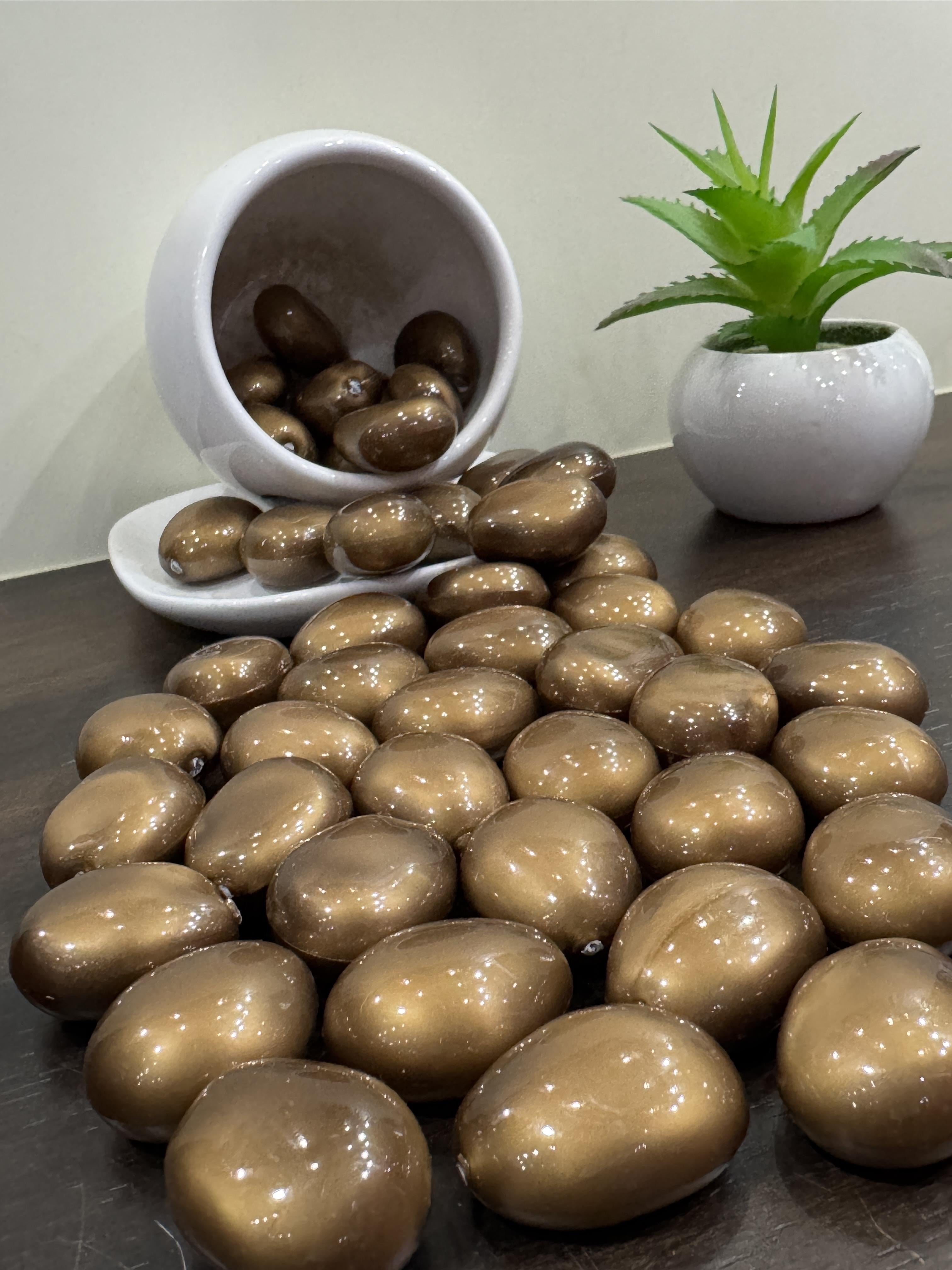 Brown pebbles on a dark surface with a white bowl and plant in the background.