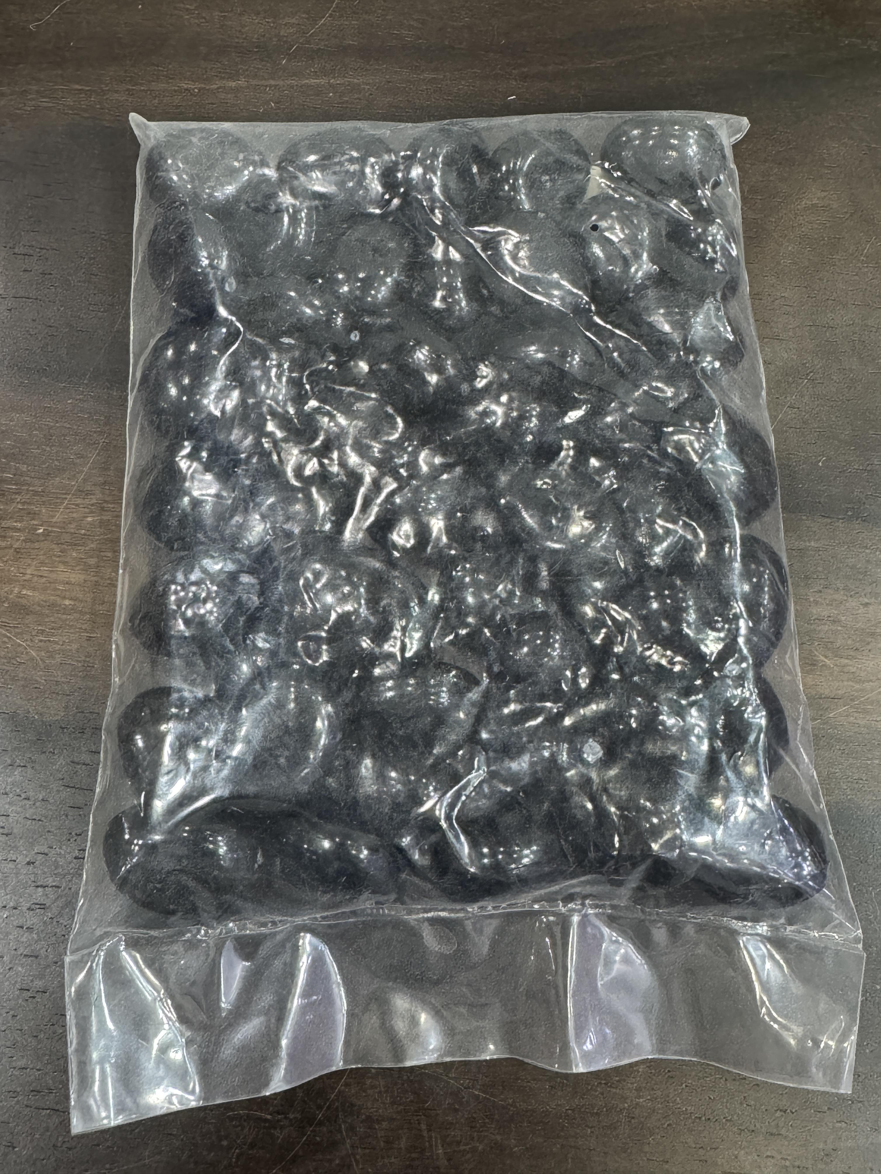 Clear plastic bag filled with black pebbles on a wooden surface