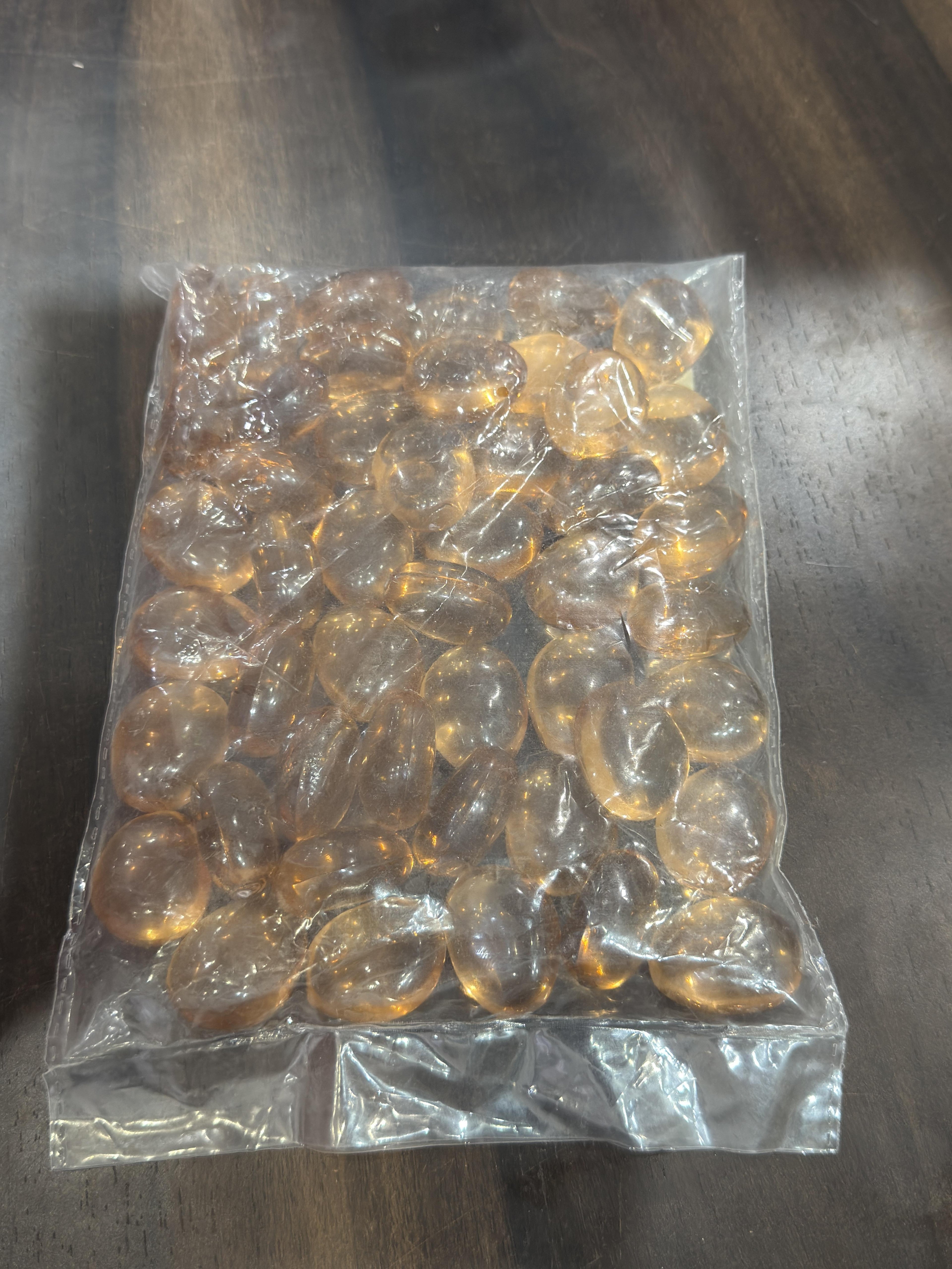 Clear plastic bag filled with amber-colored beads on a reflective surface.
