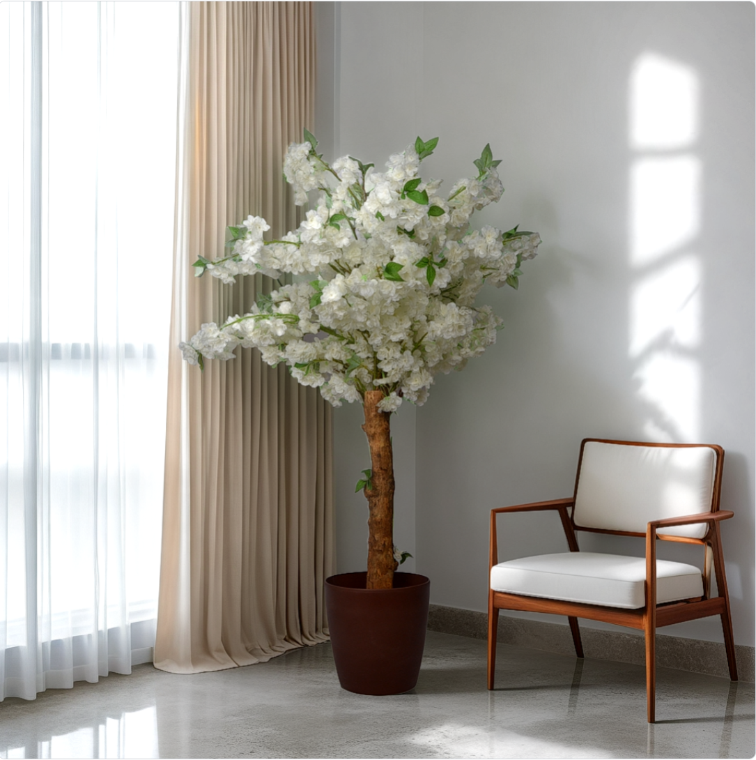A 5 foot artificial cherry blossom plant with white flowers, placed in a room corner next to a window, beside a wooden chair with a white cushion.