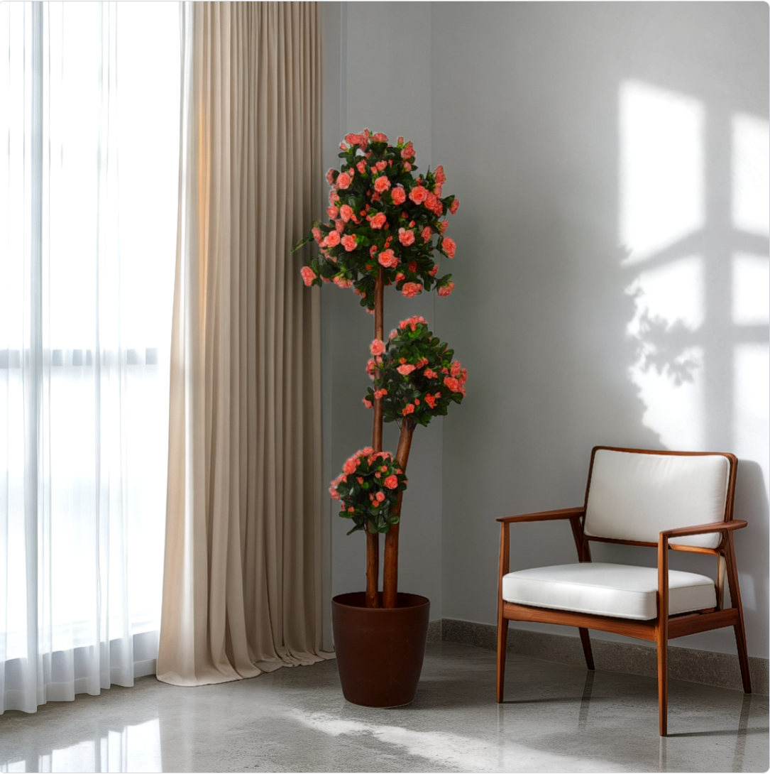 A 5 ft artificial azalea flower plant with green leaves and pink blooms, placed in a brown pot, positioned next to a window with curtains in an interior setting with a chair.