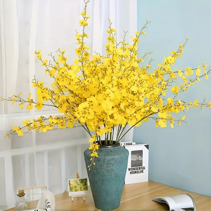 Yellow flowers in a green vase on a table with a light blue wall and white curtains in the background.