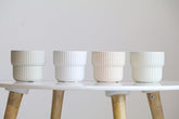 Four white ceramic pots on a white surface with wooden legs against a light gray background