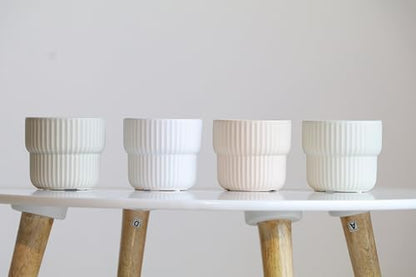 Four white ceramic pots on a white surface with wooden legs against a light gray background