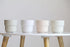 Four white ceramic pots on a white surface with wooden legs against a light gray background