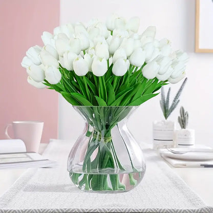 Clear glass vase with white tulips on a table with a pink wall background