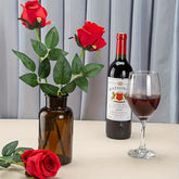 Red roses in a vase, bottle of wine, and glass on a table with a gray curtain background