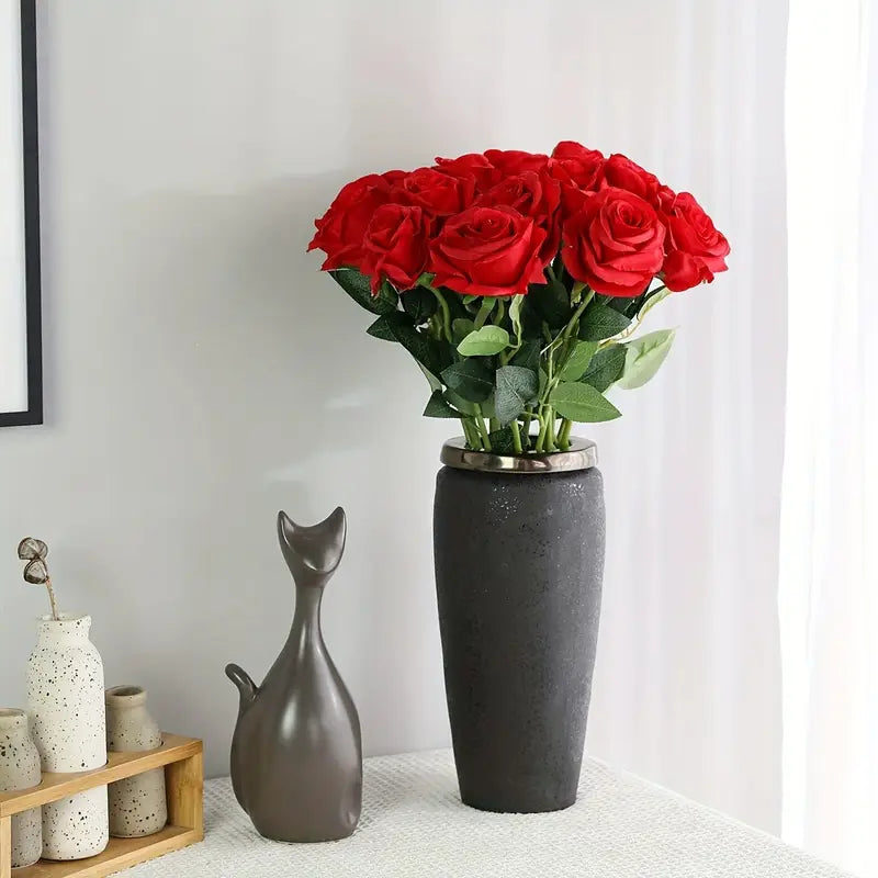 Gray vase with red roses on a white surface with decorative items.