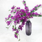 Purple bougainvillea artificial flowers in a dark vase on a white background