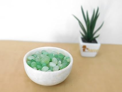 White bowl filled with green beads on a wooden surface with a plant in the background