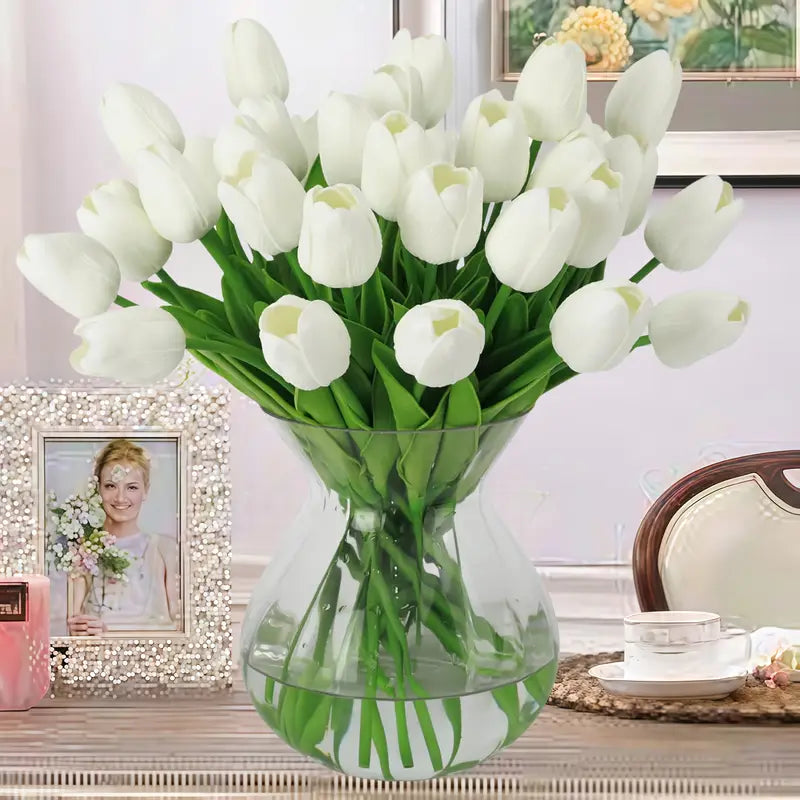 White tulips in a clear vase on a decorative table with a blurred background