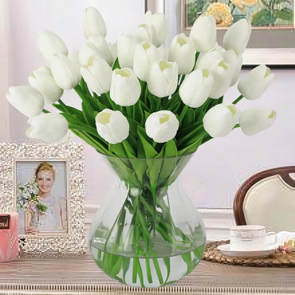 White tulips in a clear vase on a decorative table with a blurred background