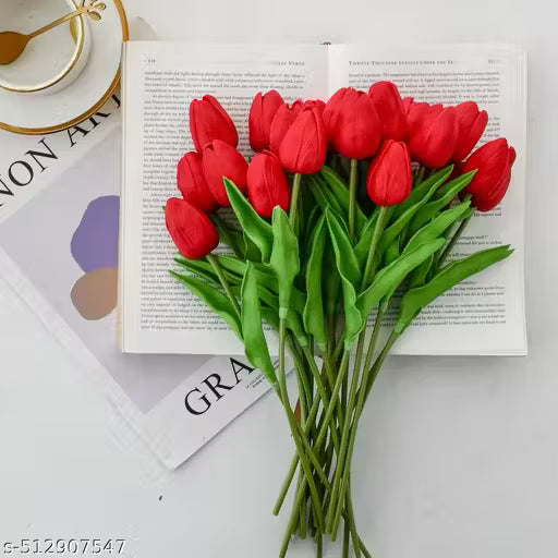 Bouquet of red tulips on an open book with a cup and saucer in the background.