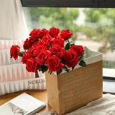 Bouquet of red roses in a paper bag on a table with a window in the background