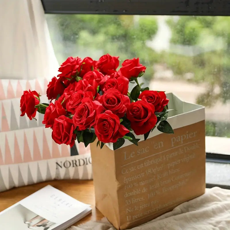 Bouquet of red roses in a paper bag on a table with a window in the background