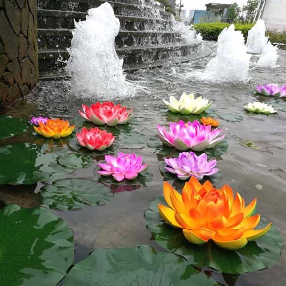Colorful artificial water lilies floating on a pond with a fountain in the background.