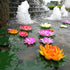 Colorful artificial water lilies floating on a pond with a fountain in the background.
