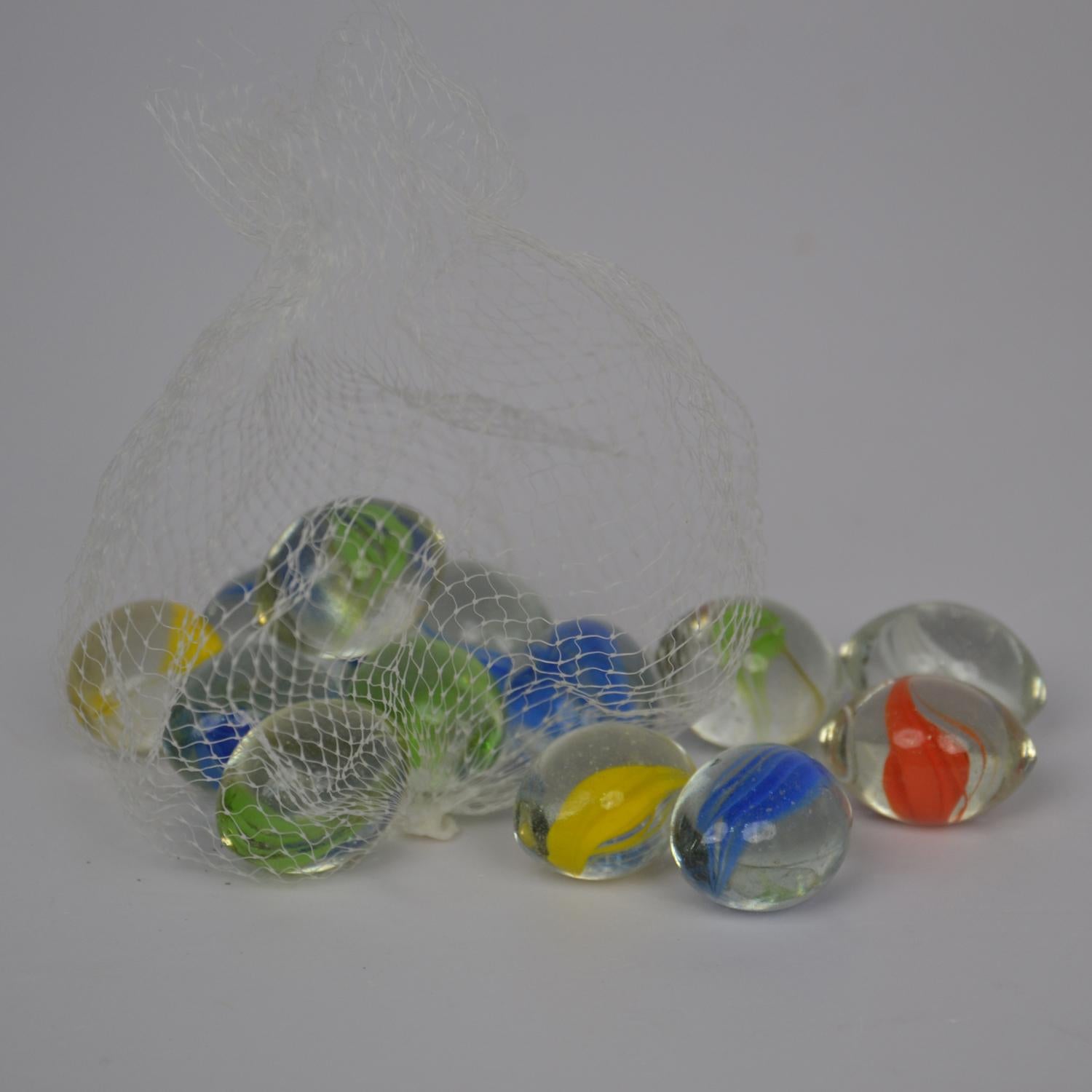 Colorful marbles spilling out of a clear plastic bag on a gray background
