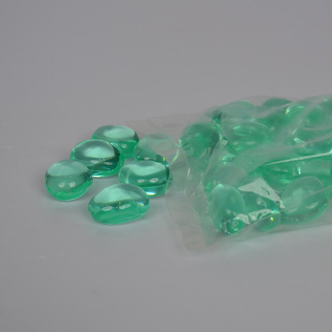 Green pebbles spilling out of a clear plastic bag on a gray background
