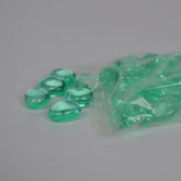 Green pebbles spilling out of a clear plastic bag on a gray background