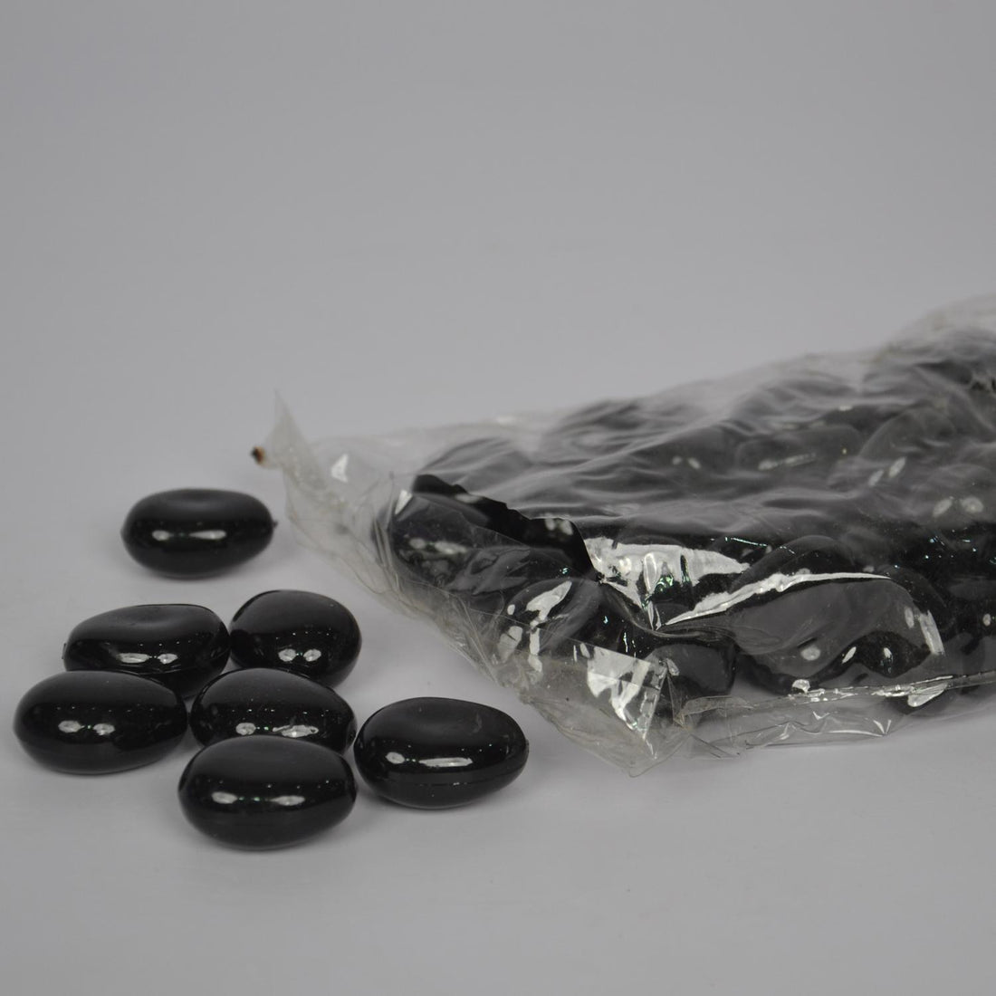 Black beans spilling out of a clear plastic bag on a gray background