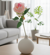 White vase with pink flower on a wooden table in a living room