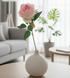 White vase with pink flower on a wooden table in a living room