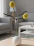 Yellow flowers in a white vase on a wooden coffee table in a living room.