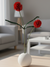 Red flowers in a white vase on a wooden table in a living room.