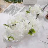 White flowers with green leaves on a white surface with magazines and a bottle.