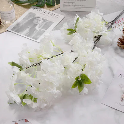 White flowers with green leaves on a white surface with magazines and a bottle.