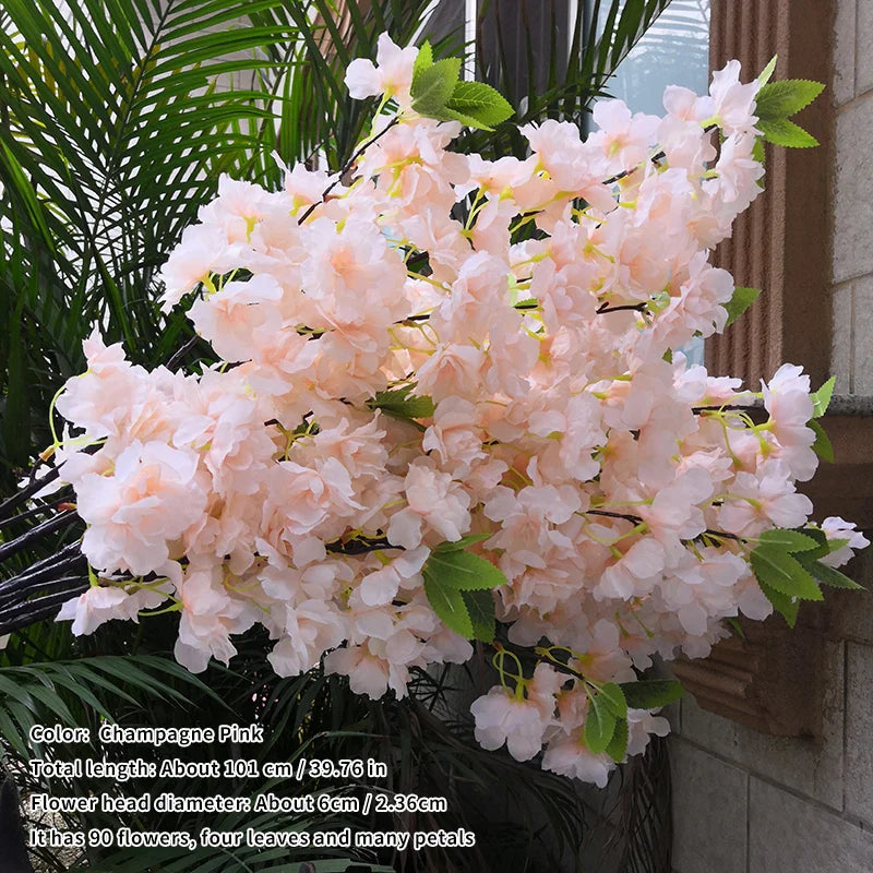 Artificial cherry blossom branch with pink flowers and green leaves on a neutral background.