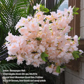 Artificial cherry blossom branch with pink flowers and green leaves on a neutral background.