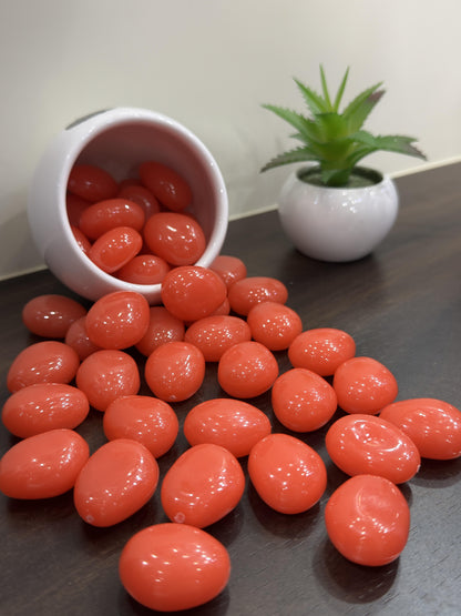 Orange pebbles on a dark surface with a white container and plant in the background.
