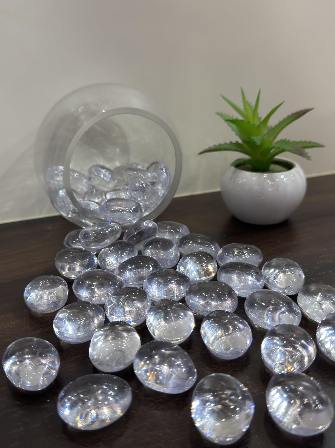 Clear decorative stones on a dark surface with a transparent container and a small plant in the background.