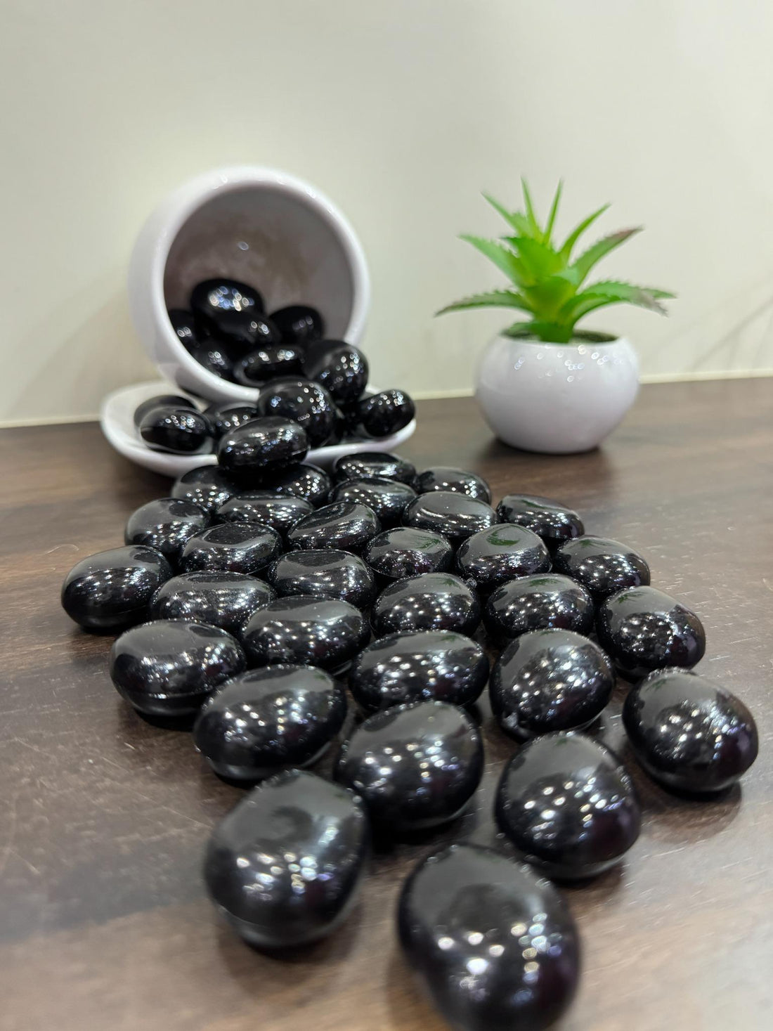Black stones on a wooden surface with a small white bowl and green plant in the background.