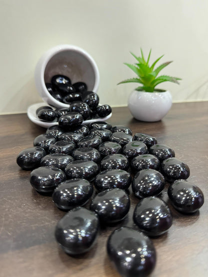Black stones on a wooden surface with a small white bowl and green plant in the background.