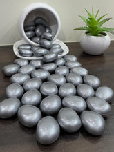 Gray pebbles on a dark surface with a white container and plant in the background.