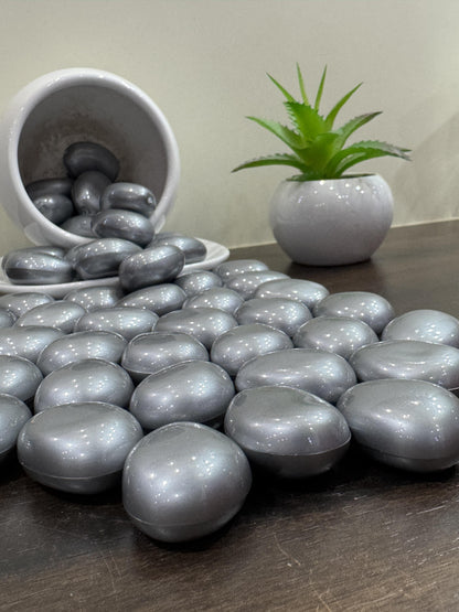 Silver metallic stones on a wooden surface with a small plant in the background.