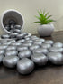 Silver metallic stones on a wooden surface with a small plant in the background.