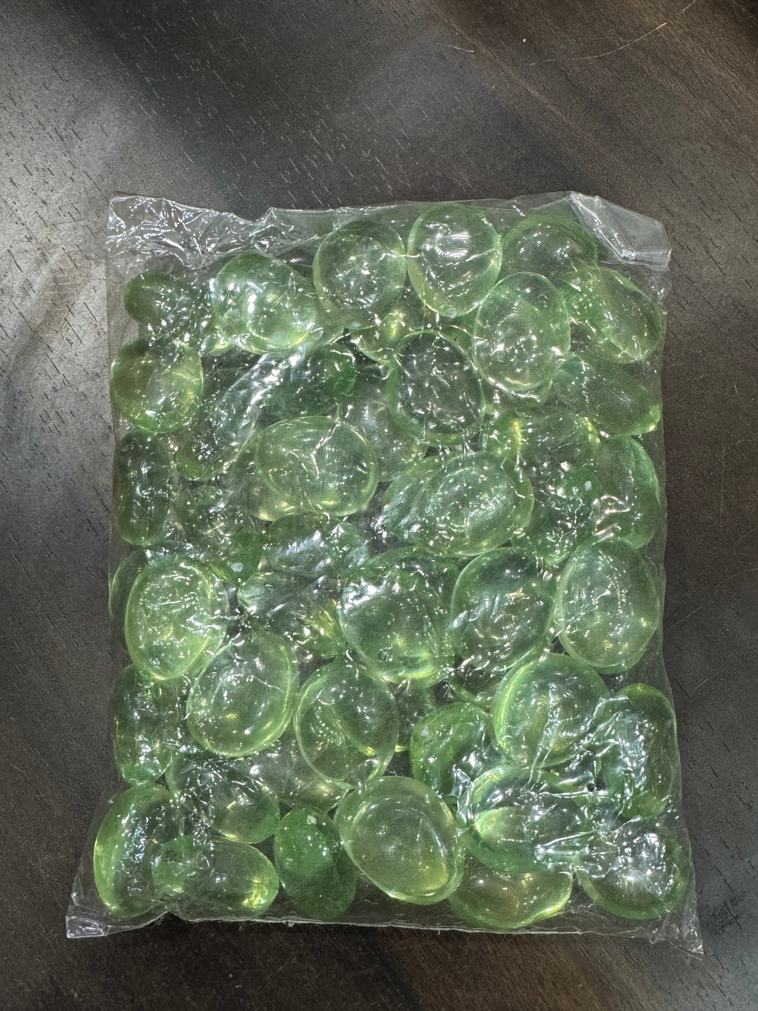 Clear plastic bag filled with green beads on a dark surface