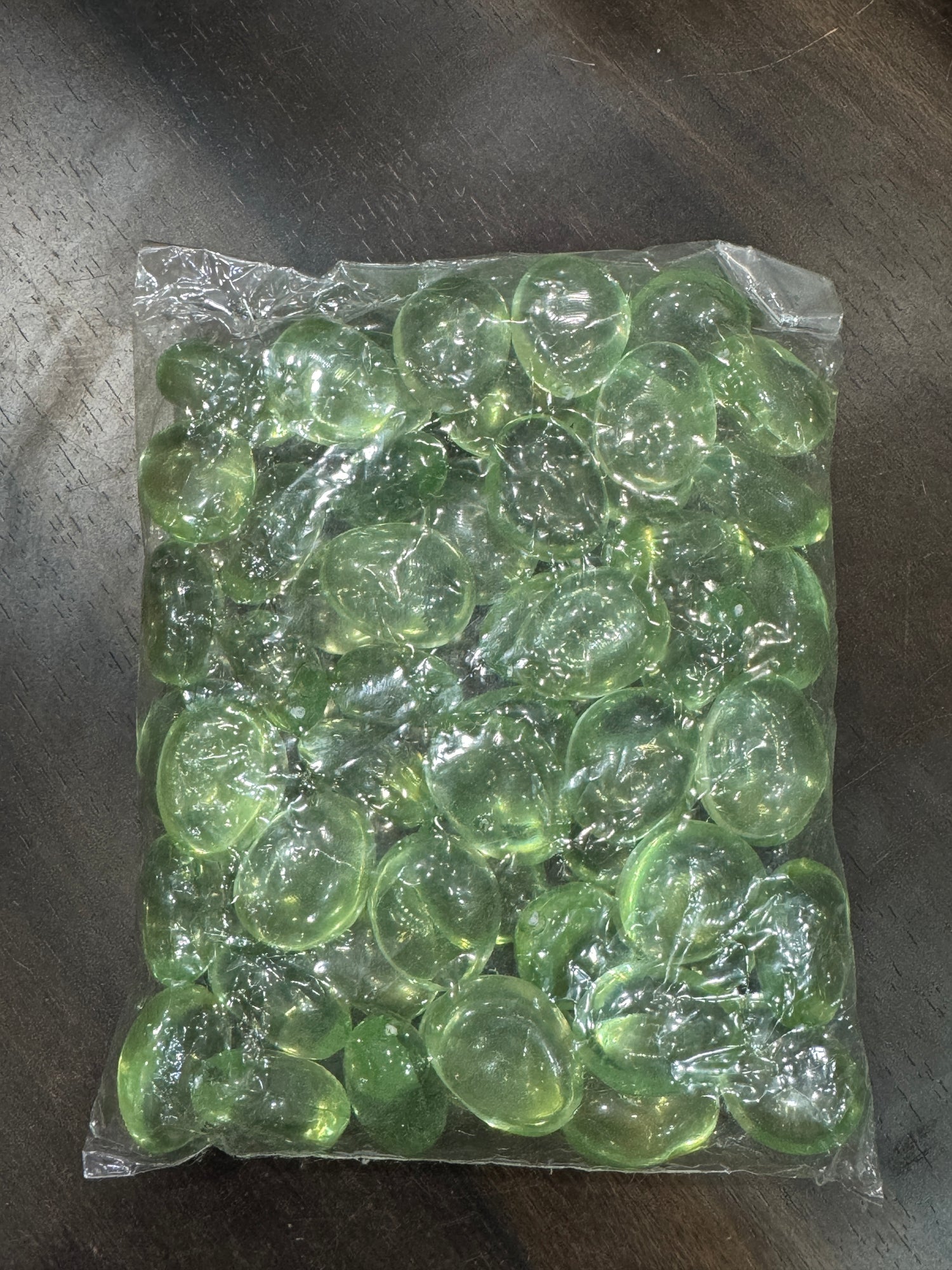 Clear plastic bag filled with green beads on a dark surface