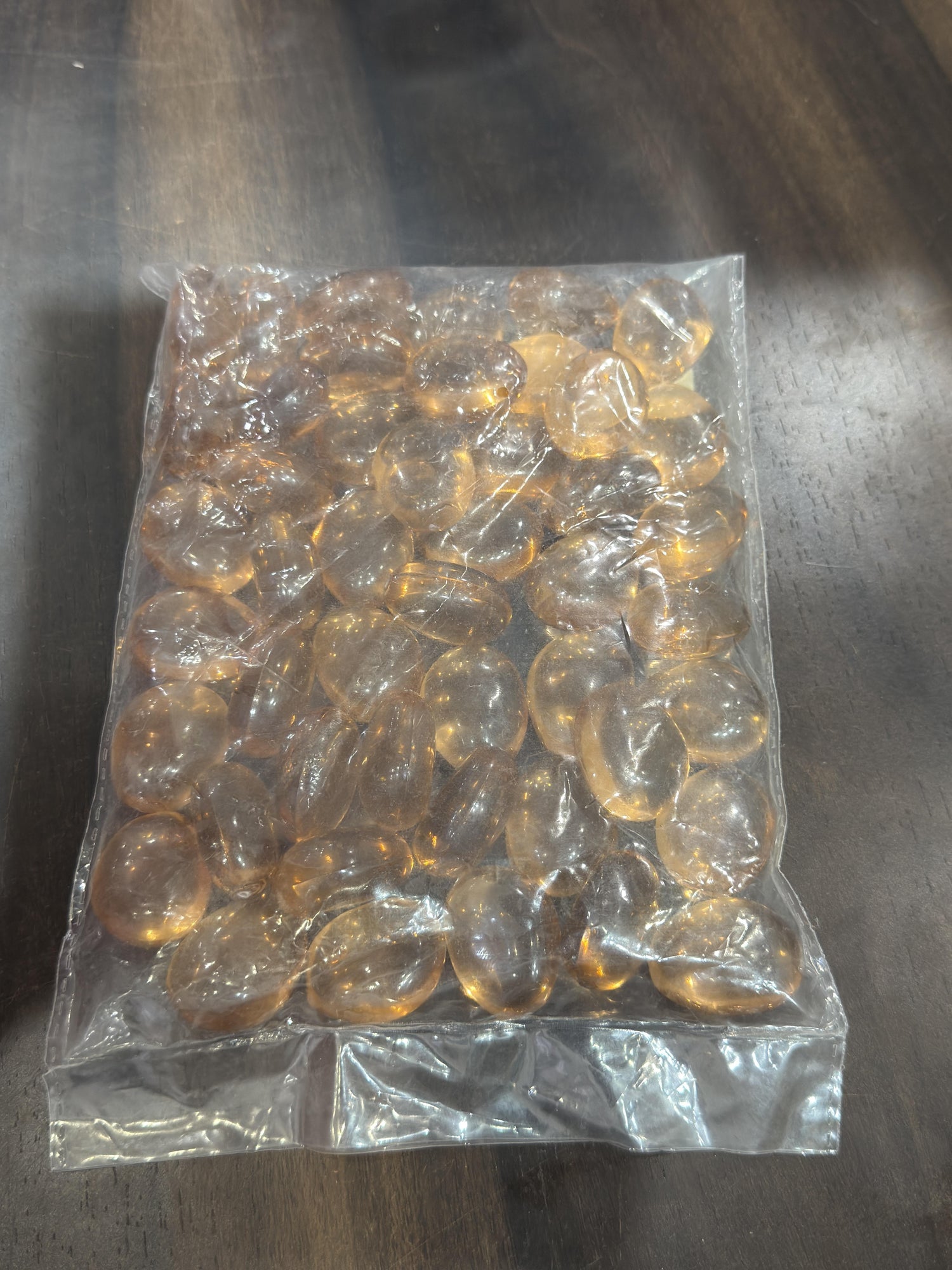 Clear plastic bag filled with amber-colored beads on a reflective surface.