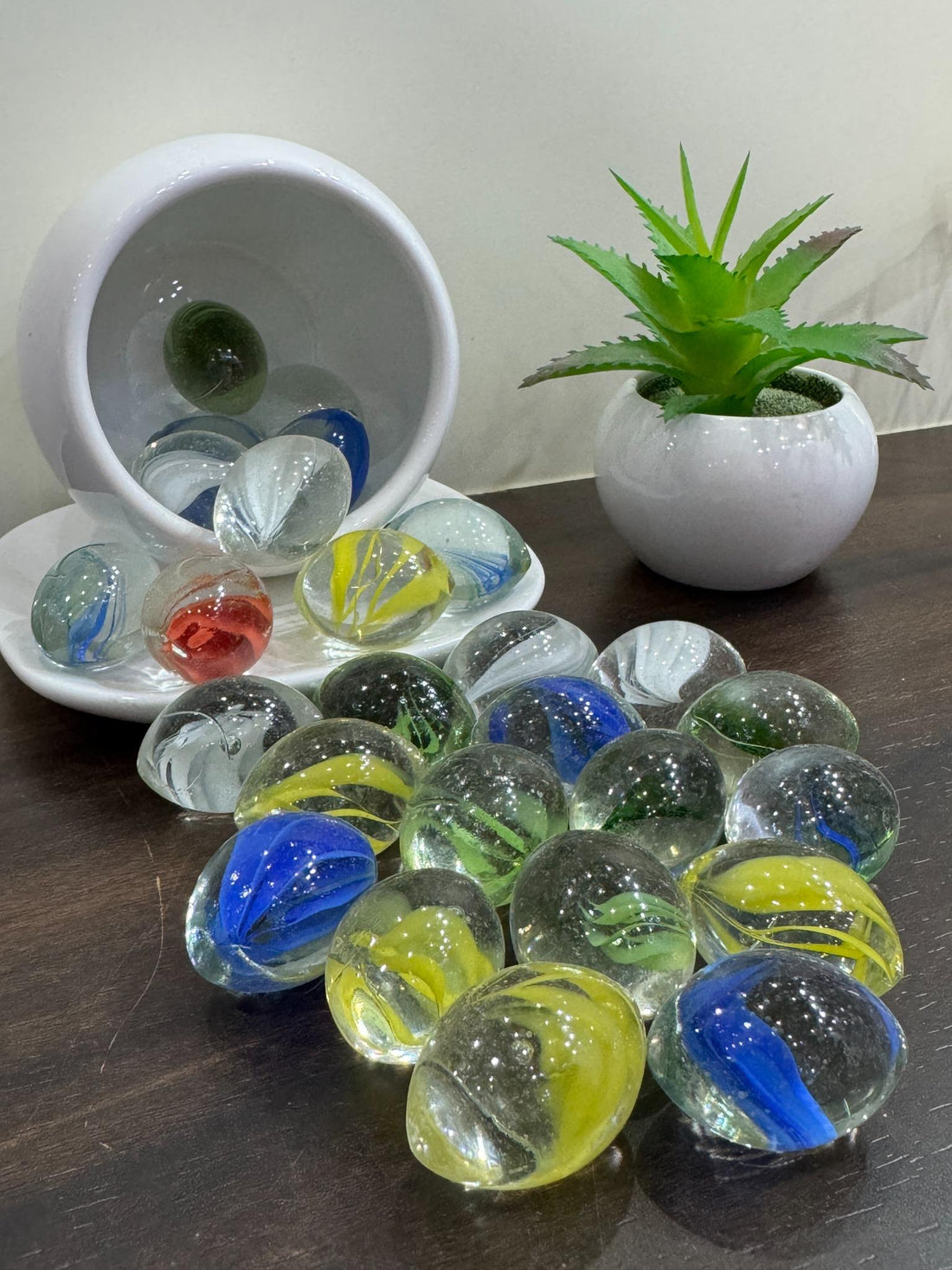 Colorful glass marbles on a table with a small potted plant in the background.