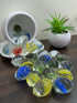 Colorful glass marbles on a table with a small potted plant in the background.