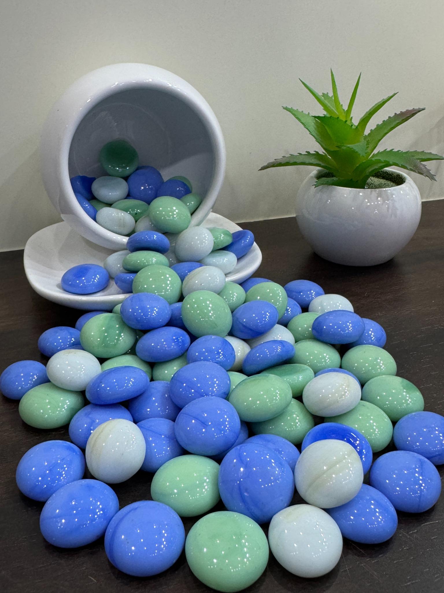 Colorful marbles in a white container with a plant on a dark surface